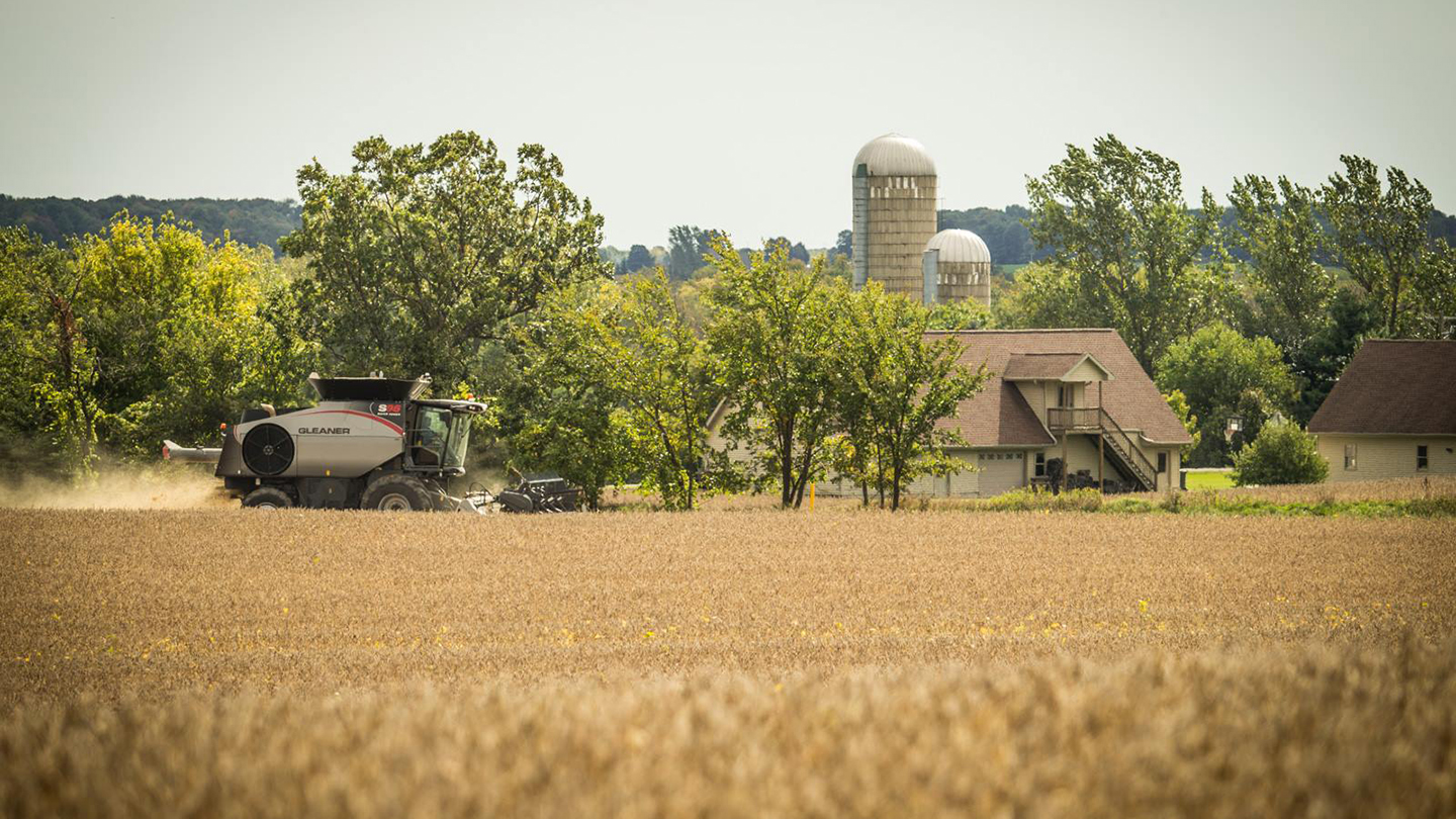 Gleaner Combine in a field in front of a farm